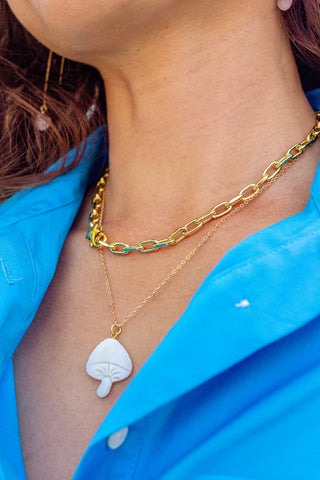 Close-up of a person wearing a gold chain necklace with a white pendant, against a blue shirt.