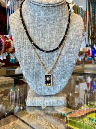 Necklace with black beads and a pendant on a gray bust in a store setting