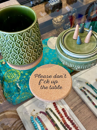 Green ceramic mug and decorative items on a table with a humorous coaster.