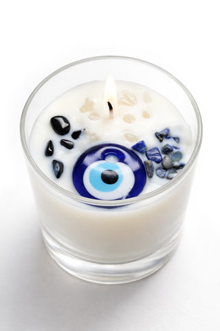 Candle in a glass container with evil eye bead and other stone elements on a white background