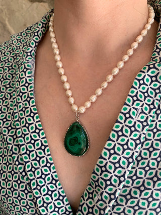 Pearl necklace with a green malachite pendant worn by a person in a patterned outfit.