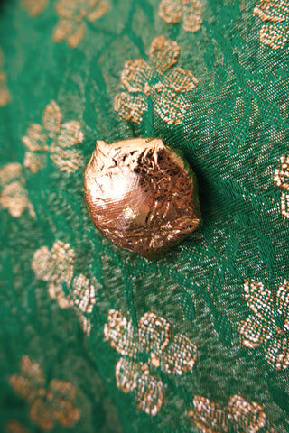 Gold metallic button on a green fabric with gold clover patterns.