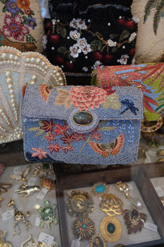 Decorative beaded handbag with floral and butterfly patterns on a table with jewelry items.