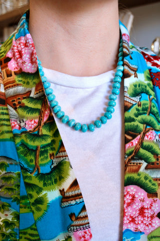 Person wearing a colorful kimono with floral patterns and a turquoise necklace.