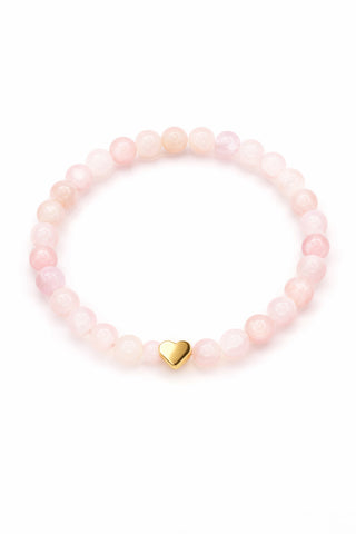 Pink rose quartz beaded bracelet with a gold heart charm on a white background