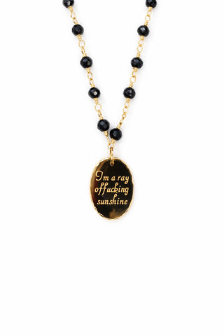 Rosary style necklace with black beads and a gold pendant on a white background