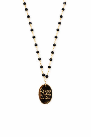 Rosary style necklace with black beads and a gold pendant on a white background