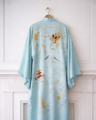 Light blue embroidered kimono on a hanger against a white paneled wall.