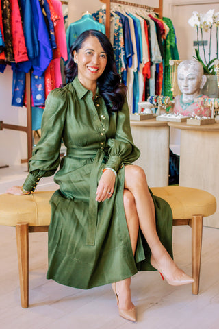 Woman in a green dress sitting on a bench in a clothing store.