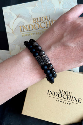 Close up of a wrist wearing a black beaded bracelet with pavé charm and 'Bijou Indochine' jewelry box in the background