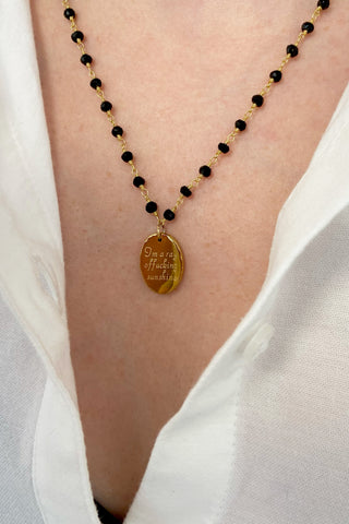 Rosary necklace with black beads and a gold pendant on a white shirt background