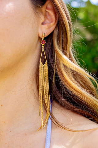 Close up of ear wearing gold fringe earring with ruby.