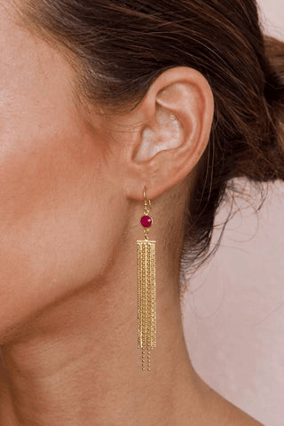 Gold tassel earring with a red gemstone worn by a person.