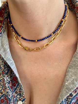 Necklace with blue lapis beads and gold star chain on a person wearing a patterned garment.