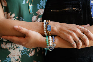 Close-up of hands wearing multiple bracelets and rings with a blurred floral background