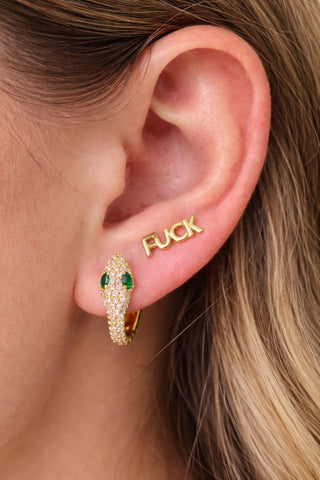Gold snake earring with green gemstone eyes worn by a person, close-up of ear.